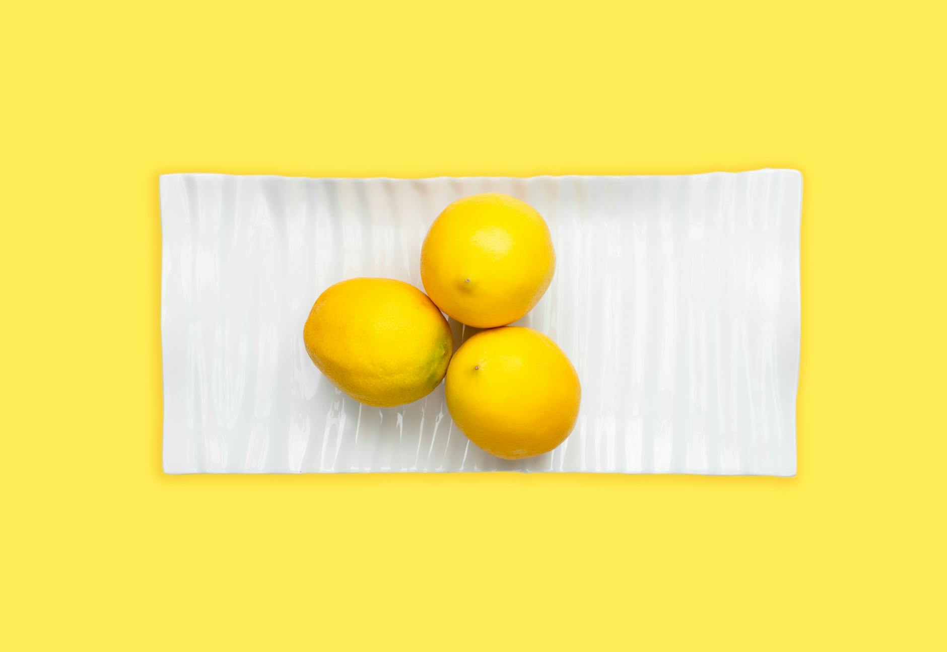 Fresh lemons arranged on a white plate with vibrant yellow background, symbolizing renewal and restored sensation
