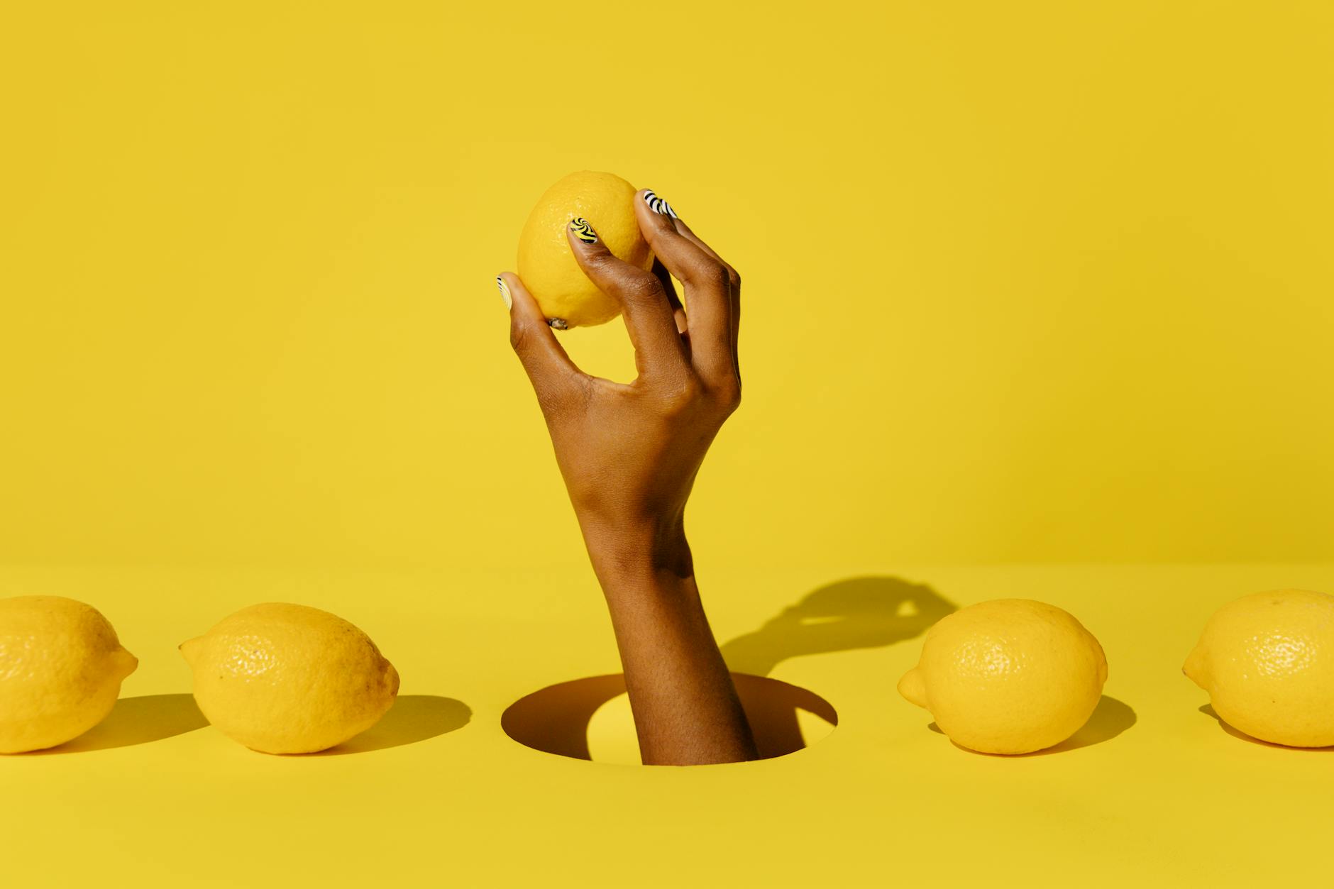 A hand holding a fresh lemon against a bright yellow background, representing renewal and fresh starts