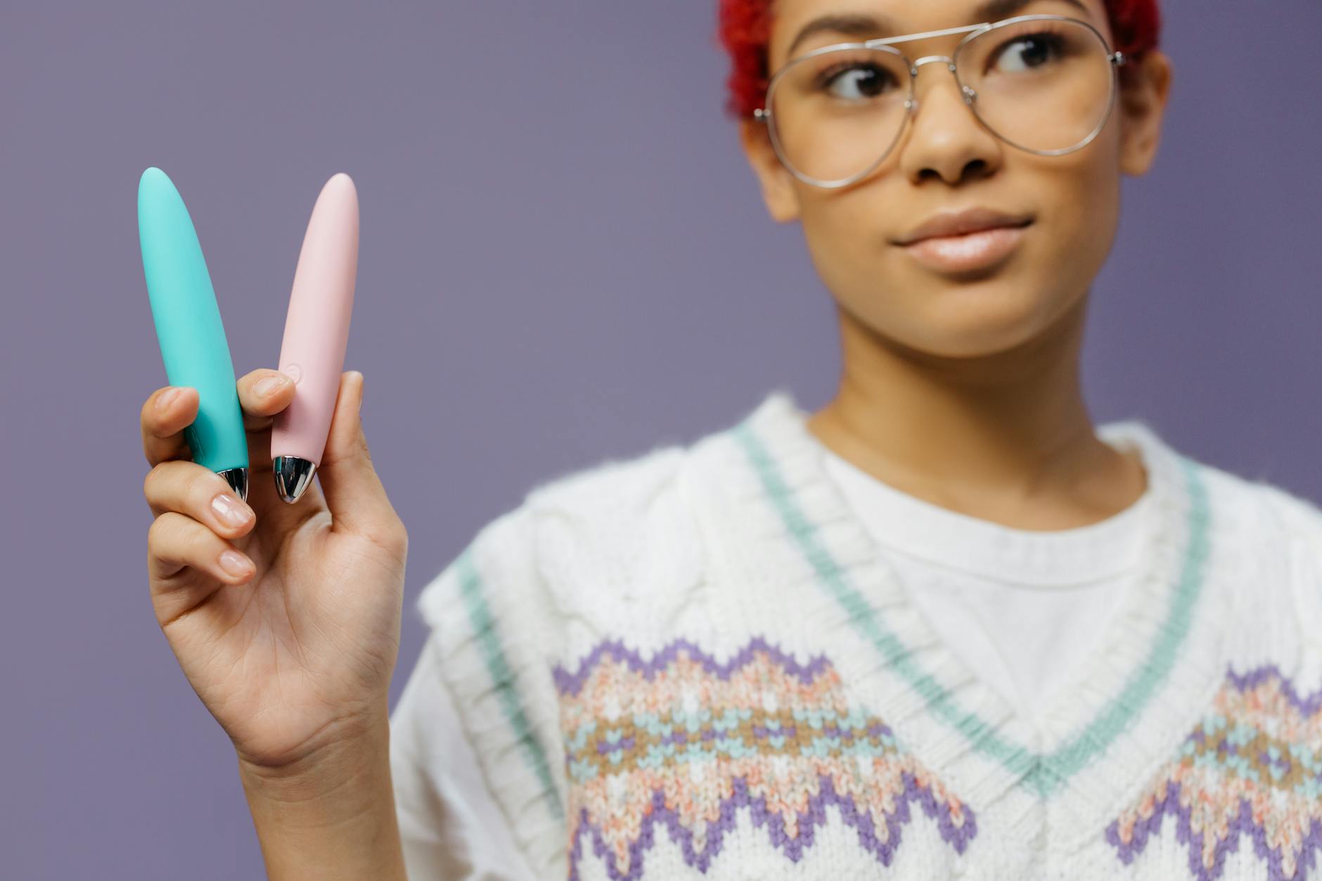 A woman holding colorful vibrators against a purple background, showing options for gentle clitoral pleasure