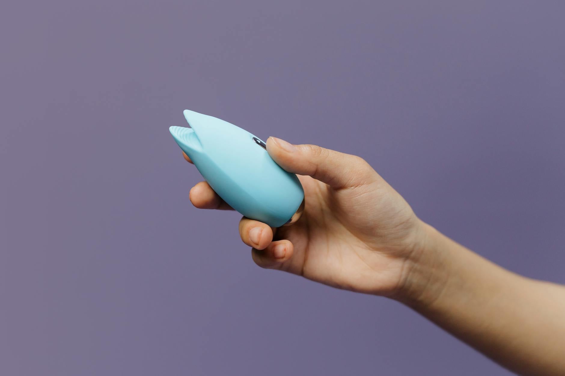 A blue silicone clitoral vibrator held in hand, symbolizing self-pleasure and sexual wellness for mature women