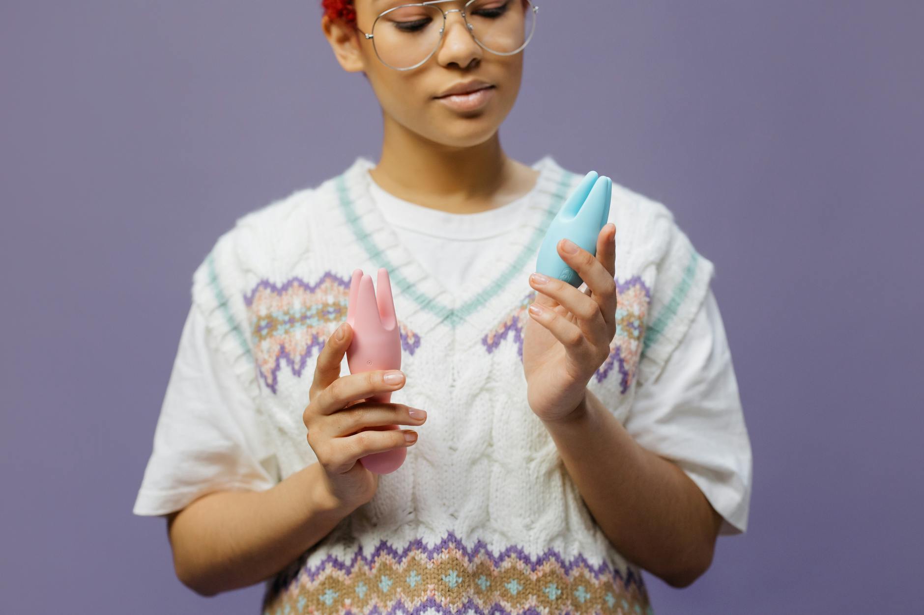Woman holding blue and pink silicone vibrators with a contemplative expression