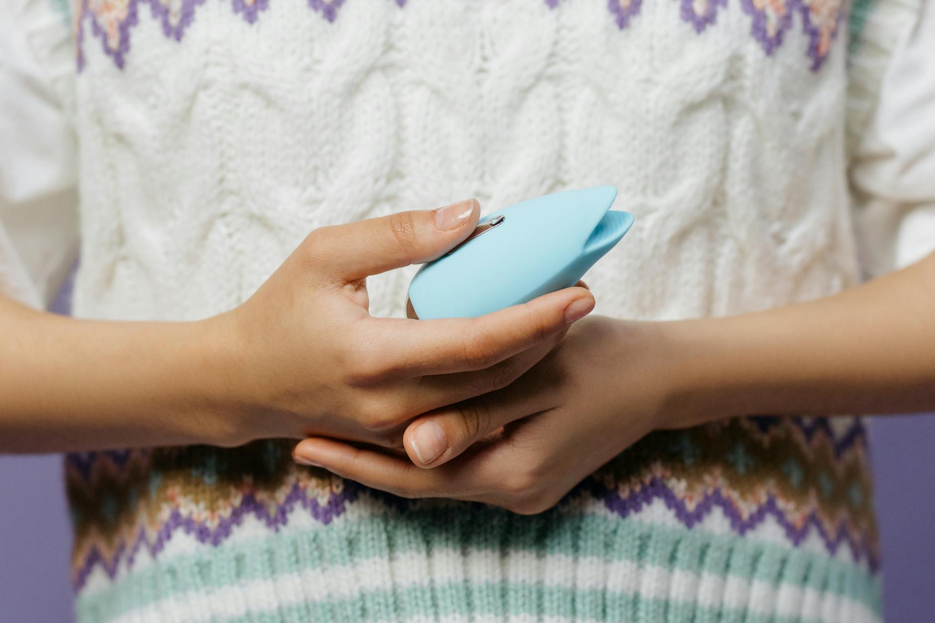 Una mano sostiene un masajeador personal azul contra un suéter de punto, mostrando confort e intimidad