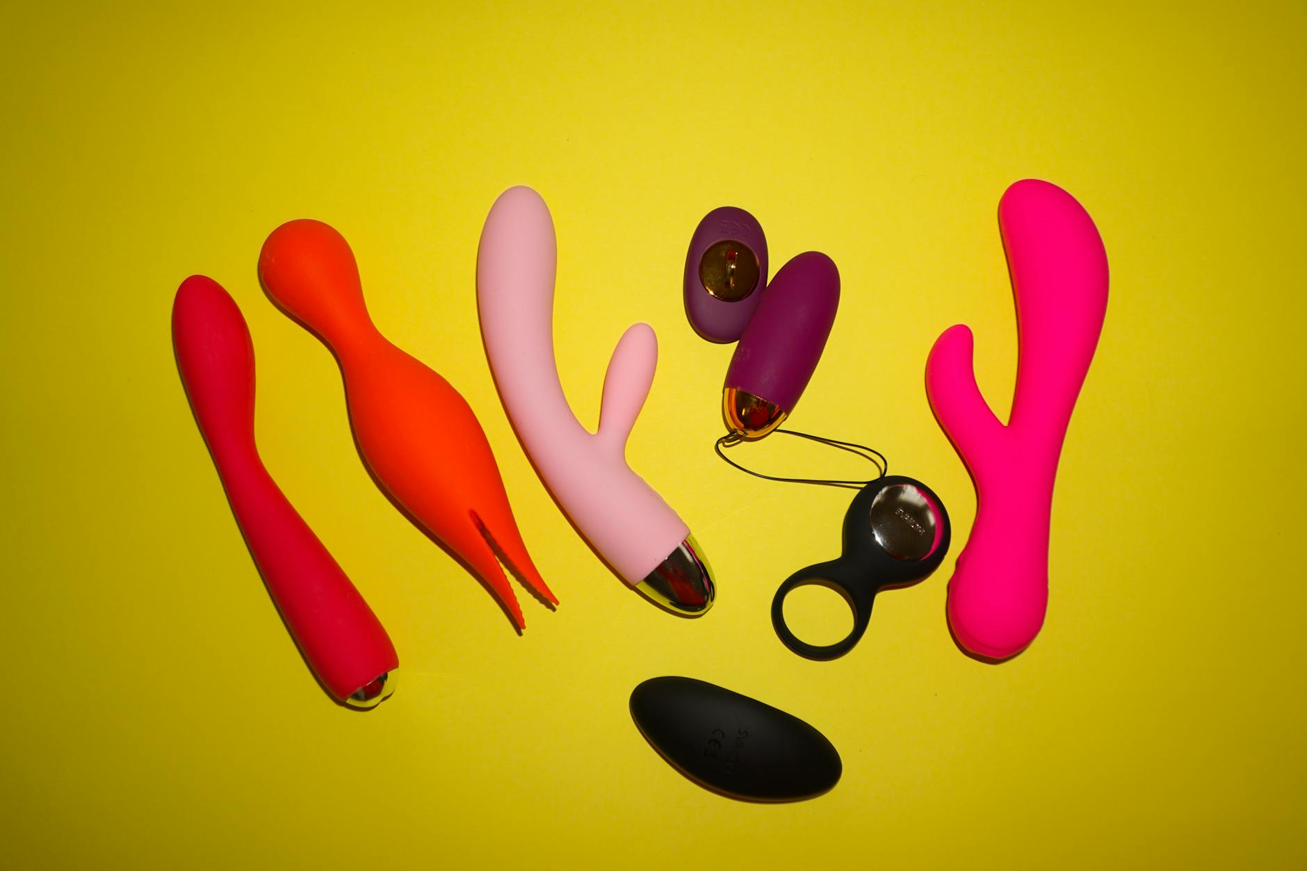 Colorful vibrators and intimate items arranged on a bright yellow background, representing diverse pleasure options